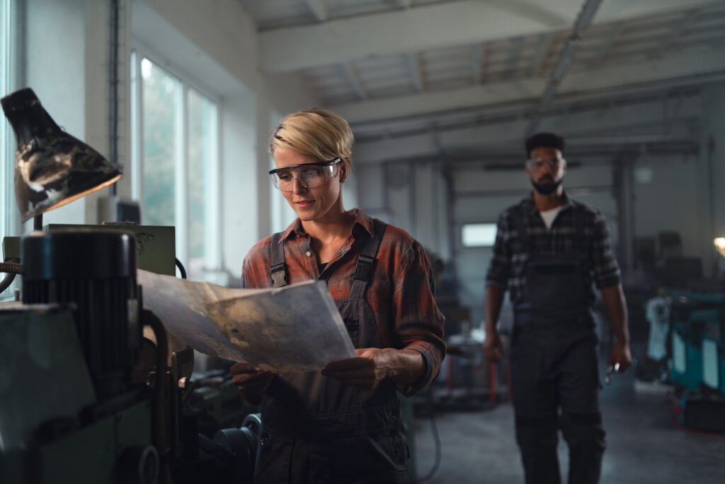 Portrait of young biracial industrial colleagues working indoors in metal workshop, smiling
